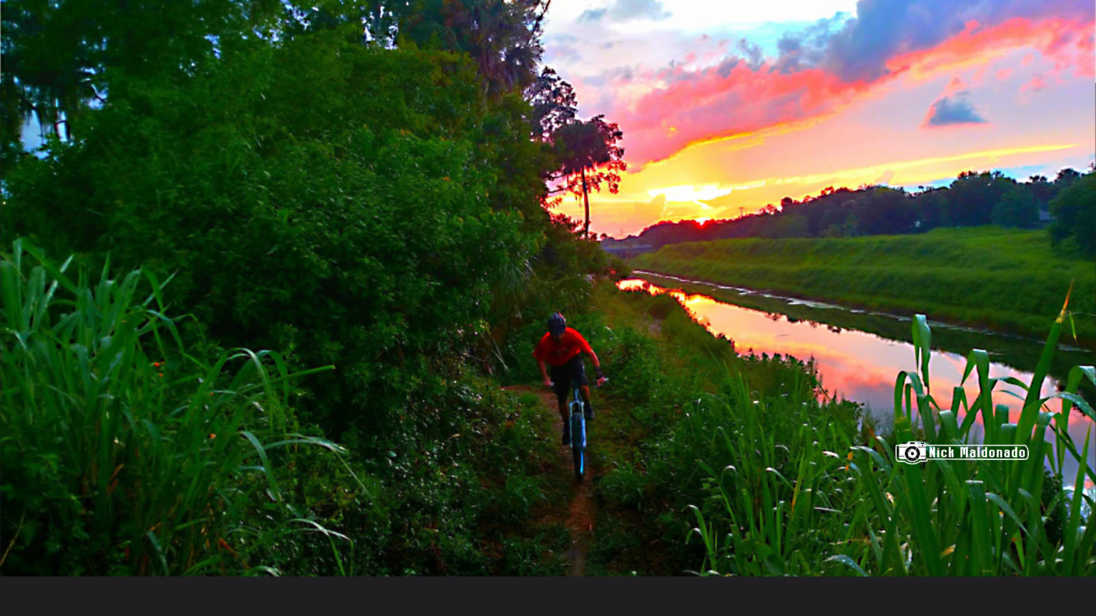 Person cycling on a MTB along the Tillman canal in Palm Bay, FL with a colorful sunset sky.
